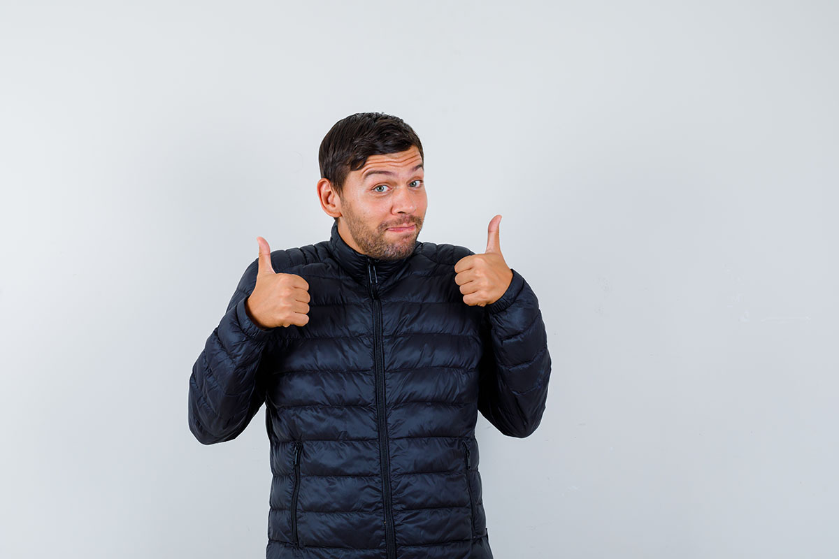 young male showing double thumbs up in puffer jacket and lookin